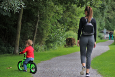 A woman walks on a trail next to her young son who is riding a bike